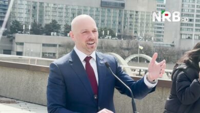 Bald man in a blue suit and red tie speaks into a microphone outdoors, NRB HD logo in the corner.