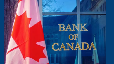 Canadian flag beside a blue glass Bank of Canada building with gold lettering on the facade.