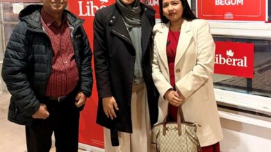 Three people pose indoors in front of red Liberal banners at a campaign event.