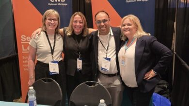 Four people pose together at a CWB Optimum Mortgage booth with blue-and-orange banners in the background and a candy bowl on the table below them.