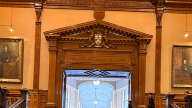 Ornate wood doorway labeled Legislative Library, crest above, leading to a lit hallway with portraits on the walls.