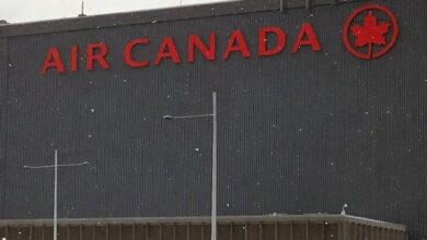 Air Canada sign on a dark building wall with red letters reading 'AIR CANADA' and a red maple leaf logo, snowy scene.