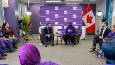 Panel discussion in a SEIU Healthcare room with two speakers seated in armchairs in front of a purple backdrop, Canadian flag on the right, cameras set up, and a small audience in purple attire seated in a semicircle.