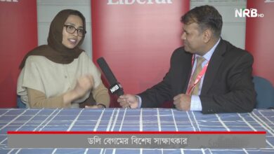 Woman in a brown hijab and glasses being interviewed by a man in a suit; NRB HD microphone between them, red backdrop behind them.