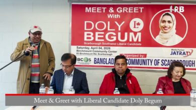 Man in tan coat speaks into a microphone at a meet-and-greet with Doly Begum, Liberal candidate, banner in background.