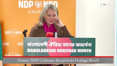 Speaker at a podium during an Ontario NDP Bangladeshi Heritage Month event, with an orange NDP backdrop and microphones in front of her.