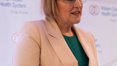 Woman in a beige blazer speaks at a transparent podium against a backdrop with William Osler Health System logos.
