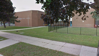 Brick school building with a cross emblem on the wall, green lawn, and a sidewalk framing the scene.