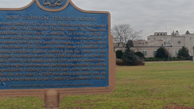 Blue historical information sign about the RCAF Technical Training School in a grassy field, with a campus building visible in the background.