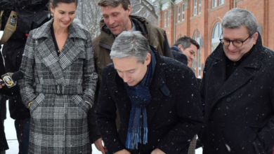 Group of adults in winter coats standing outside in the snow, with cameras filming nearby.