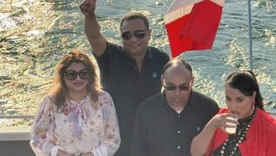 Four adults on a boat deck by the water, with a Canadian flag in the background; one man raises a peace sign while others stand nearby.