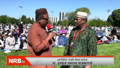 Reporter with a red microphone interviewing an imam in a green traditional robe at a large outdoor Muslim prayer gathering; NRB TV banner in the foreground.