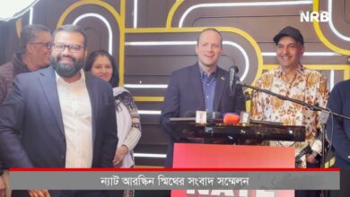 Group of officials at a press conference, man at podium speaking into multiple microphones, NRB logo visible in the background, others smiling nearby.