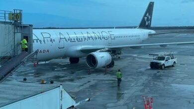 White passenger jet docked at a gate with a jet bridge attached and ground crew on a wet tarmac.