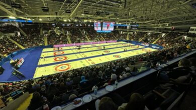 Large indoor arena filled with spectators watching a curling competition; four parallel sheets with red and yellow bullseyes and blue borders.
