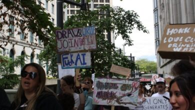 Crowd of protesters marching along a city street, holding handmade signs about human rights and social issues.