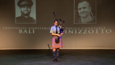 Young woman in a tartan skirt plays bagpipes on a stage, with large portrait photos projected behind and text on screen.