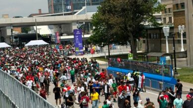 Large crowd walking along a closed street at a city event, with barriers and a crane in the background.