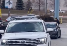 White Ford SUV in the foreground in a parking lot, with other cars and a storefront in the background.