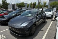 Front three-quarter view of a dark gray Tesla Model Y parked diagonally in a crowded outdoor parking lot.