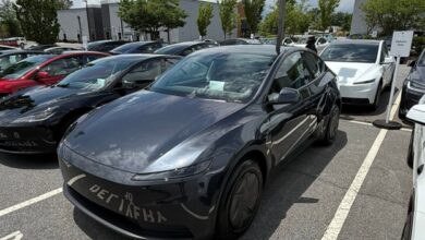 Front three-quarter view of a dark gray Tesla Model Y parked diagonally in a crowded outdoor parking lot.