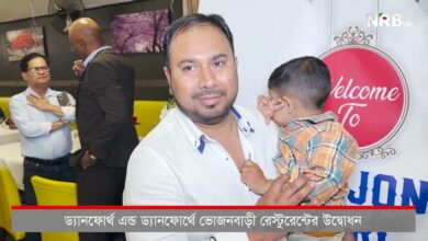 Man holding a child at a welcome event, with a large red 'Welcome' sign in the background.
