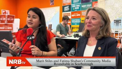 Two women sit at a table in a bright studio; a red-shirted interviewer speaks into an NRB microphone while a guest listens, with campaign posters on an orange wall behind them.