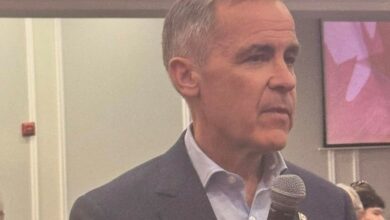 Man in a navy blazer speaking into a handheld microphone at a formal event indoors