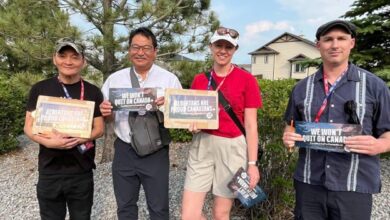 Four people stand outdoors on a gravel area, each holding signs with pro-Canada messages and smiling at the camera.