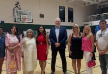 Group of eight adults standing in a gymnasium posing for a photo, dressed in semi-formal attire.
