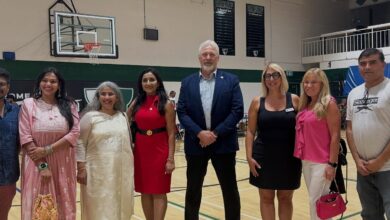 Group of eight adults standing in a gymnasium posing for a photo, dressed in semi-formal attire.